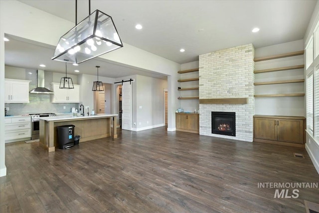 3303 S Island Fox Ave, Eagle, ID 83616 - kitchen with stainless steel gas stove, wall chimney exhaust hood, a barn door, light countertops, and dark wood-type flooring