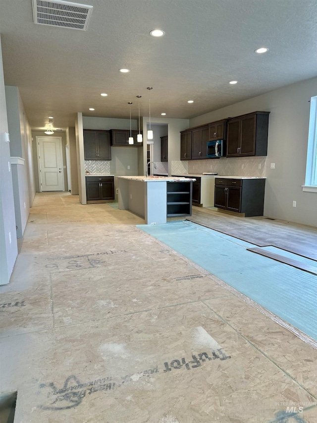 kitchen featuring tasteful backsplash, dark brown cabinets, an island with sink, and decorative light fixtures