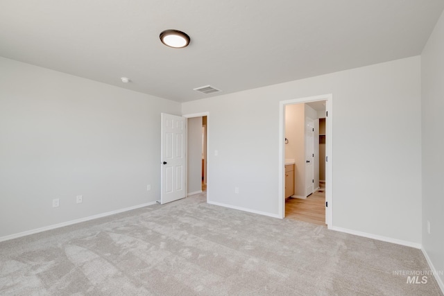 unfurnished bedroom with baseboards, visible vents, connected bathroom, and light colored carpet
