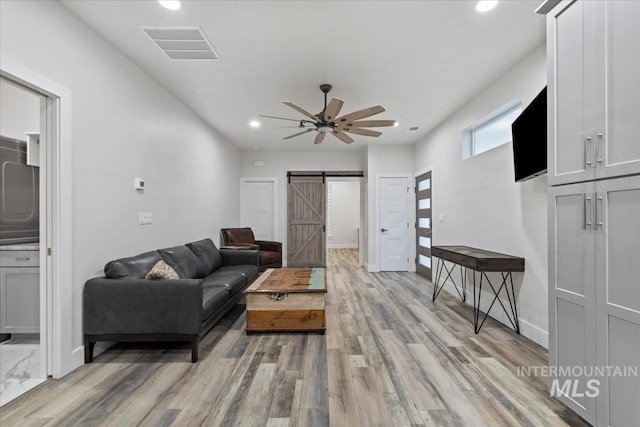 living room with ceiling fan, a barn door, and light hardwood / wood-style flooring