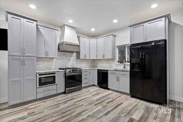 kitchen with gray cabinetry, backsplash, custom exhaust hood, and black appliances