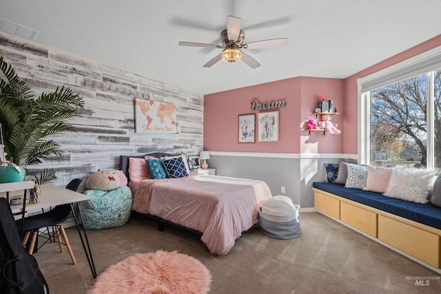 carpeted bedroom with ceiling fan and wood walls