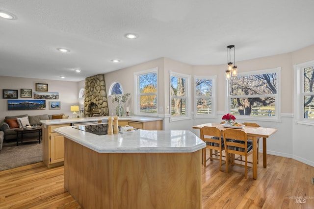 kitchen with a wealth of natural light, light stone counters, light hardwood / wood-style flooring, an island with sink, and decorative light fixtures