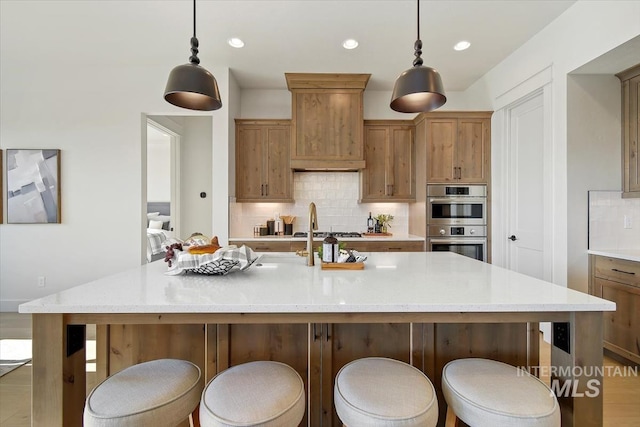 kitchen with a breakfast bar, an island with sink, hanging light fixtures, and decorative backsplash