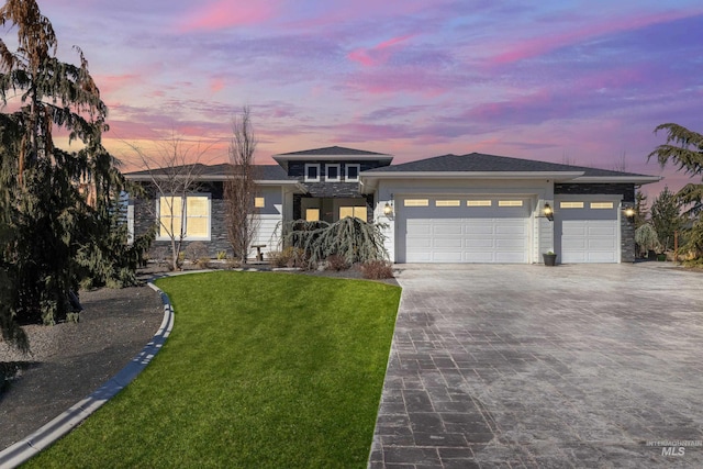 prairie-style house featuring decorative driveway, a front lawn, an attached garage, and stone siding