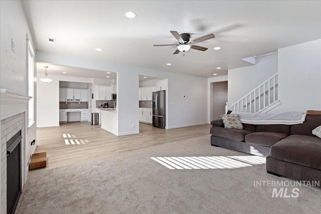 carpeted living room featuring a brick fireplace and ceiling fan