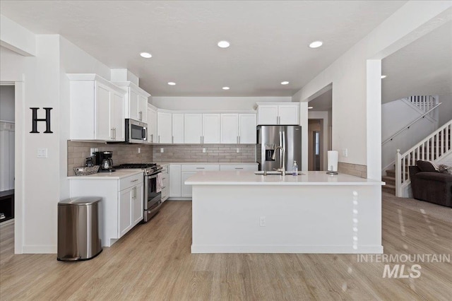 kitchen with sink, backsplash, stainless steel appliances, light hardwood / wood-style floors, and white cabinets