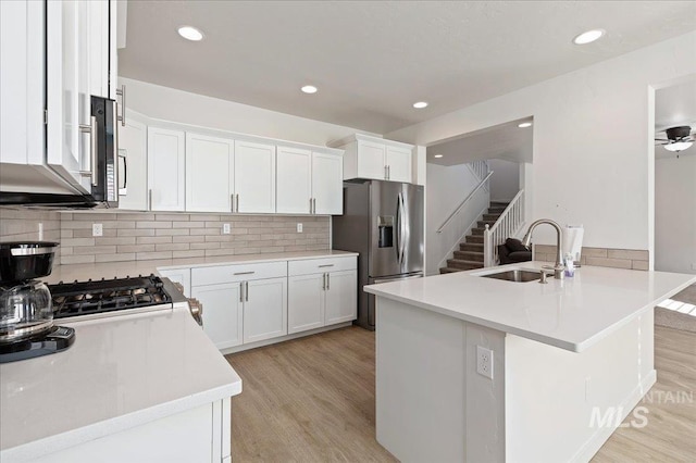 kitchen featuring stove, stainless steel fridge with ice dispenser, sink, and white cabinets