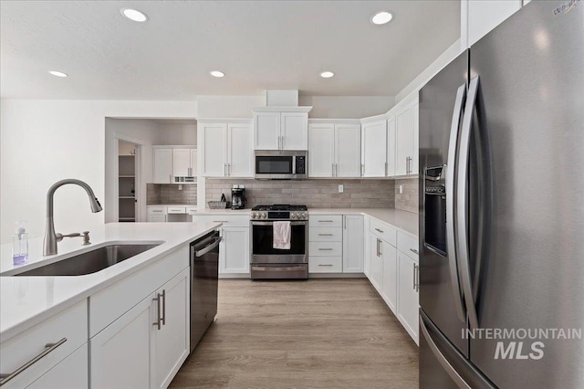 kitchen with white cabinetry, sink, backsplash, stainless steel appliances, and light hardwood / wood-style flooring