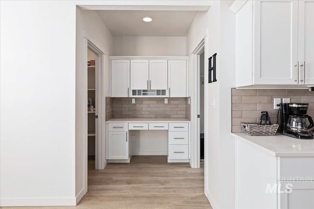 kitchen featuring built in desk, white cabinets, backsplash, and light hardwood / wood-style floors