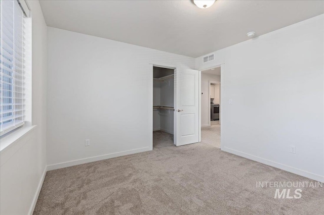 unfurnished bedroom featuring light carpet, a walk in closet, and a closet