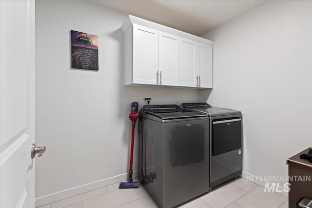 clothes washing area with cabinets, washing machine and dryer, and light tile patterned floors