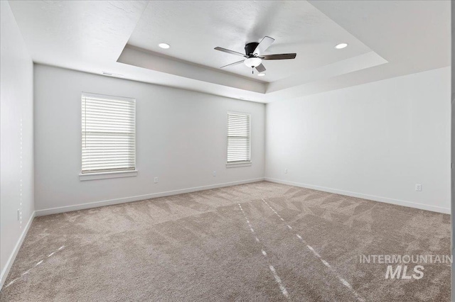 carpeted spare room with ceiling fan and a tray ceiling