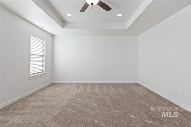 empty room featuring ceiling fan, a raised ceiling, and carpet floors