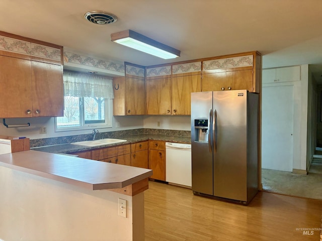 kitchen with white dishwasher, stainless steel refrigerator with ice dispenser, a sink, and brown cabinetry