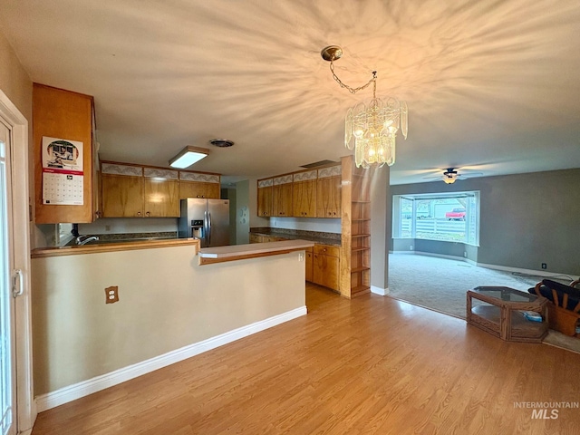 kitchen featuring open floor plan, a peninsula, brown cabinetry, and stainless steel refrigerator with ice dispenser