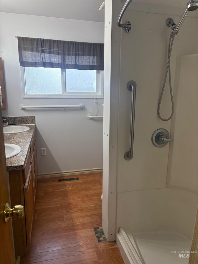 full bathroom with a shower, double vanity, visible vents, and wood finished floors