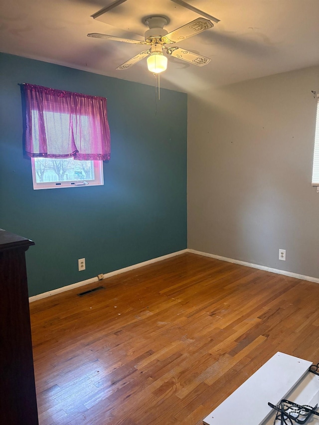 unfurnished room featuring ceiling fan, visible vents, baseboards, and wood finished floors