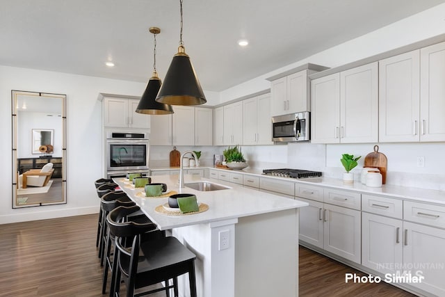 kitchen with a sink, light countertops, stainless steel appliances, dark wood-type flooring, and a kitchen bar