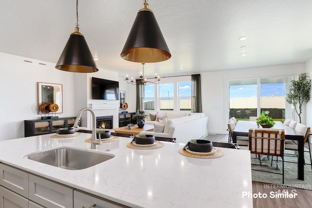 kitchen featuring pendant lighting, wood finished floors, light stone countertops, open floor plan, and a sink