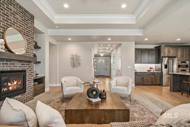 living area featuring a tray ceiling, a fireplace, light wood finished floors, and recessed lighting