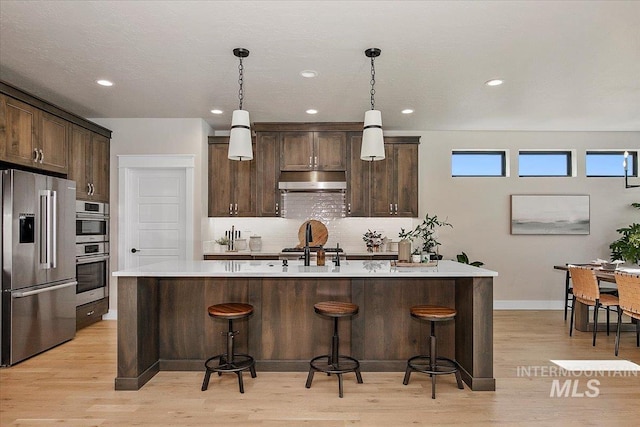 kitchen with a breakfast bar area, tasteful backsplash, appliances with stainless steel finishes, dark brown cabinets, and under cabinet range hood