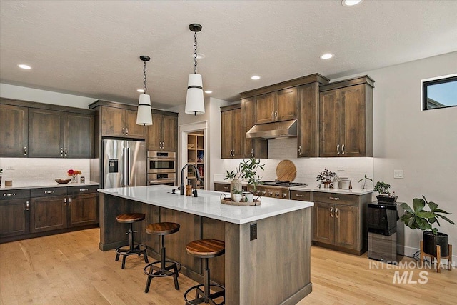 kitchen featuring stainless steel appliances, light countertops, a sink, and under cabinet range hood