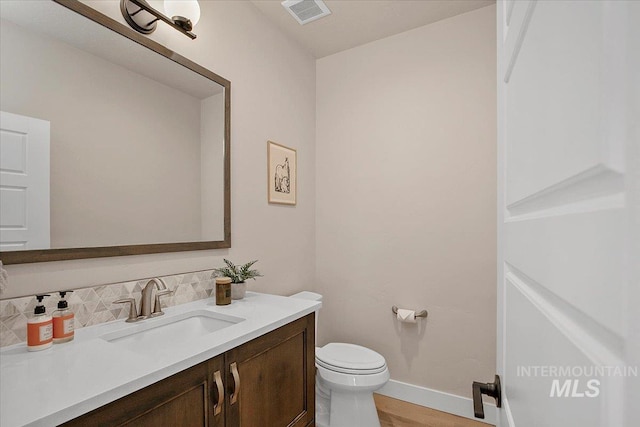 bathroom with baseboards, visible vents, decorative backsplash, toilet, and vanity