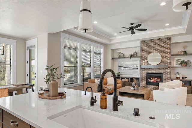 kitchen with a healthy amount of sunlight, a brick fireplace, a raised ceiling, and a sink