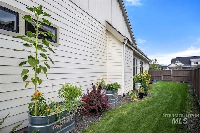 view of property exterior with board and batten siding, a yard, and fence