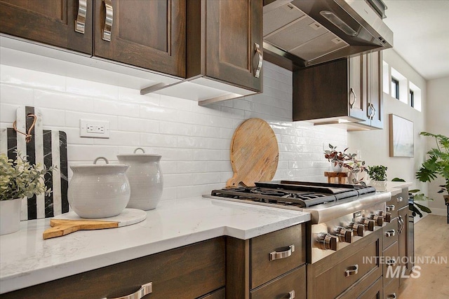 kitchen with dark brown cabinetry, tasteful backsplash, wood finished floors, under cabinet range hood, and stainless steel gas cooktop