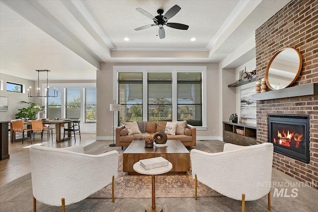 living area with a tray ceiling, a brick fireplace, a textured ceiling, baseboards, and ceiling fan with notable chandelier