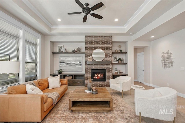 living room featuring a brick fireplace, built in shelves, a tray ceiling, and crown molding