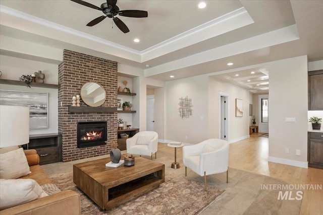 living room with light wood-style floors, recessed lighting, a raised ceiling, and a fireplace