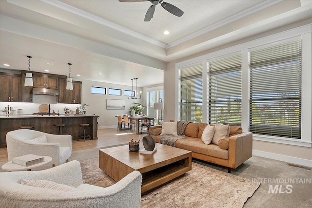 living room with baseboards, visible vents, a tray ceiling, and ornamental molding