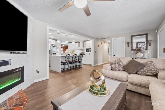 15201 Christopher, Caldwell, ID 83607 - living room featuring a ceiling fan, a textured ceiling, light wood-style floors, a tiled fireplace, and baseboards