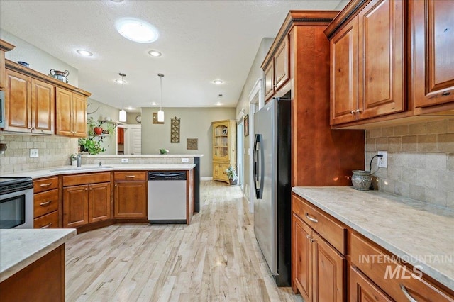 3524 Catalina Ave, Caldwell, ID 83605 - kitchen featuring appliances with stainless steel finishes, a sink, brown cabinetry, light wood finished floors, and backsplash