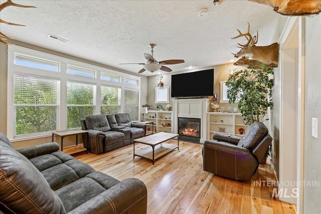3524 Catalina Ave, Caldwell, ID 83605 - living room featuring ceiling fan, light wood-type flooring, a glass covered fireplace, and a textured ceiling