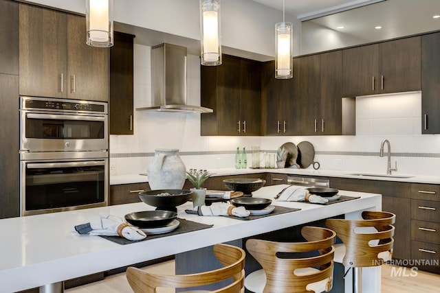 kitchen with sink, hanging light fixtures, dark brown cabinetry, stainless steel appliances, and wall chimney exhaust hood