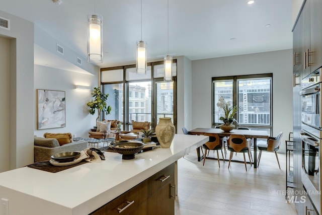 kitchen featuring a kitchen island, decorative light fixtures, dark brown cabinets, and light wood-type flooring