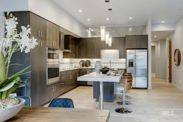 kitchen featuring dark brown cabinetry, a breakfast bar area, decorative light fixtures, a kitchen island, and stainless steel appliances