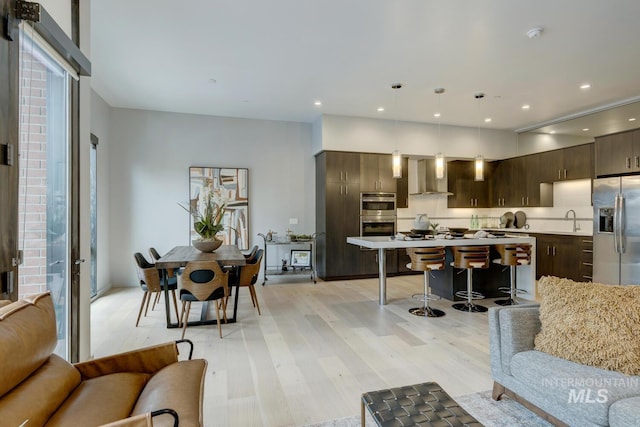 interior space featuring wall chimney exhaust hood, dark brown cabinetry, sink, hanging light fixtures, and stainless steel appliances