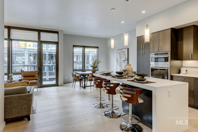 kitchen with a breakfast bar, light hardwood / wood-style floors, a kitchen island, decorative light fixtures, and stainless steel double oven