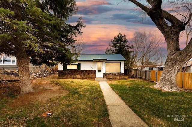 view of front of house with a front yard, fence, stone siding, and metal roof