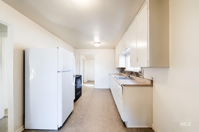 kitchen featuring a sink, white cabinets, light countertops, and freestanding refrigerator