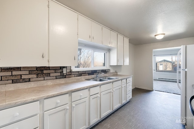 kitchen featuring a baseboard radiator, plenty of natural light, a sink, light countertops, and white cabinetry