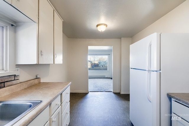 kitchen with baseboards, freestanding refrigerator, light countertops, white cabinetry, and baseboard heating