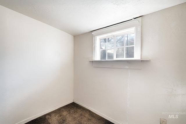 spare room with baseboards and dark colored carpet