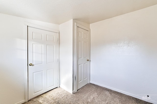 unfurnished bedroom featuring baseboards, light carpet, and a textured ceiling