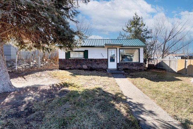 view of front of property featuring stone siding, metal roof, a front yard, and fence